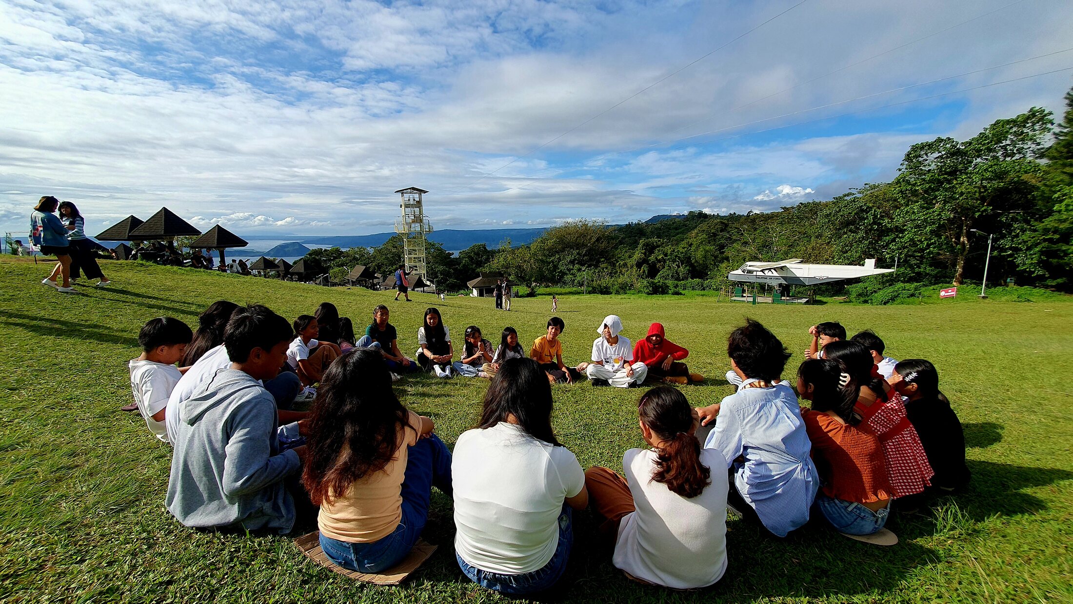 A group seated in a circle outdoors with a mountain view